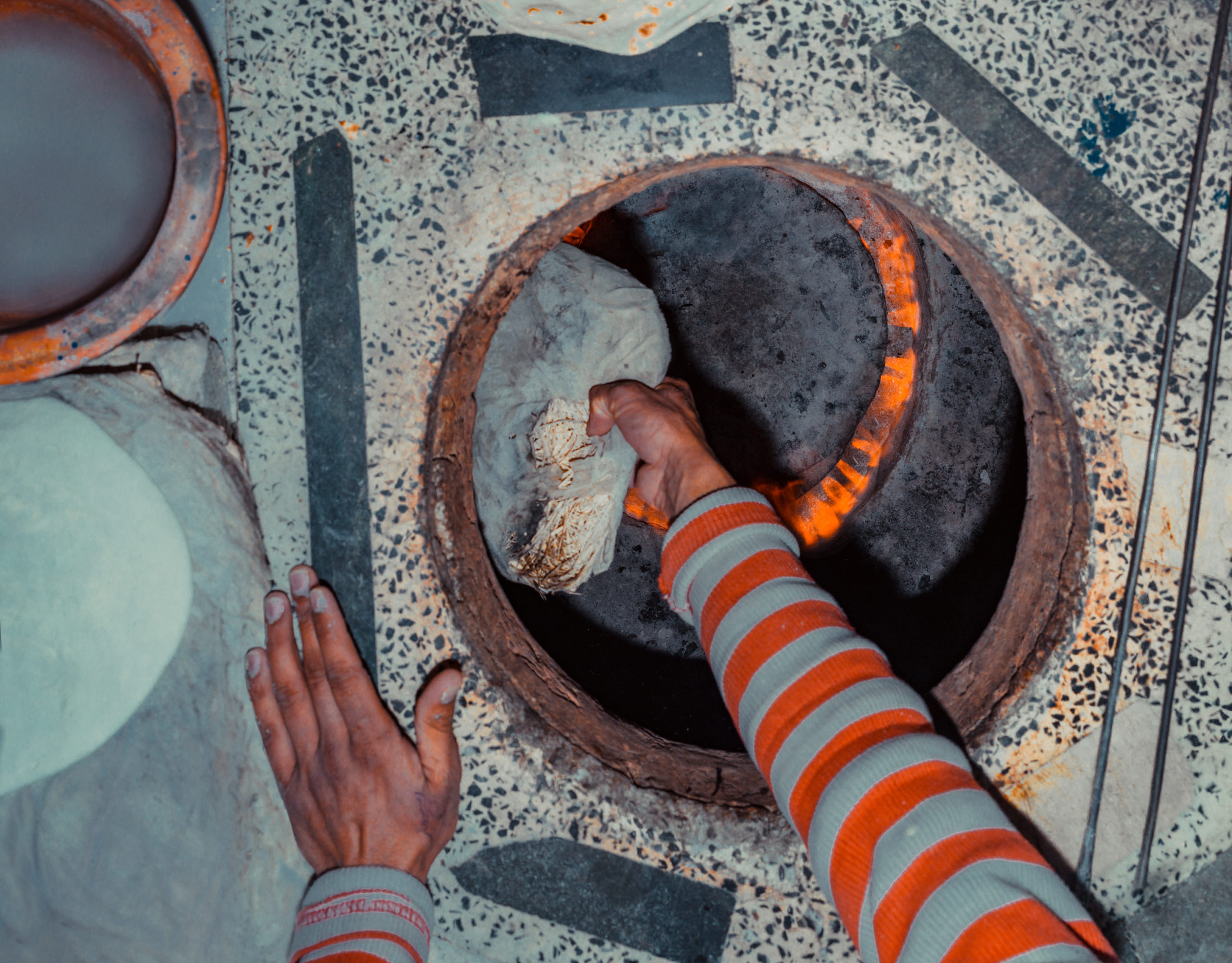A worker wearing a striped shirt leaps into the oven to place dough on the oven wall